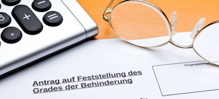 Ein Taschenrechner und eine Brille neben einem Antrag auf Feststellung des Grad der Behinderung GdB